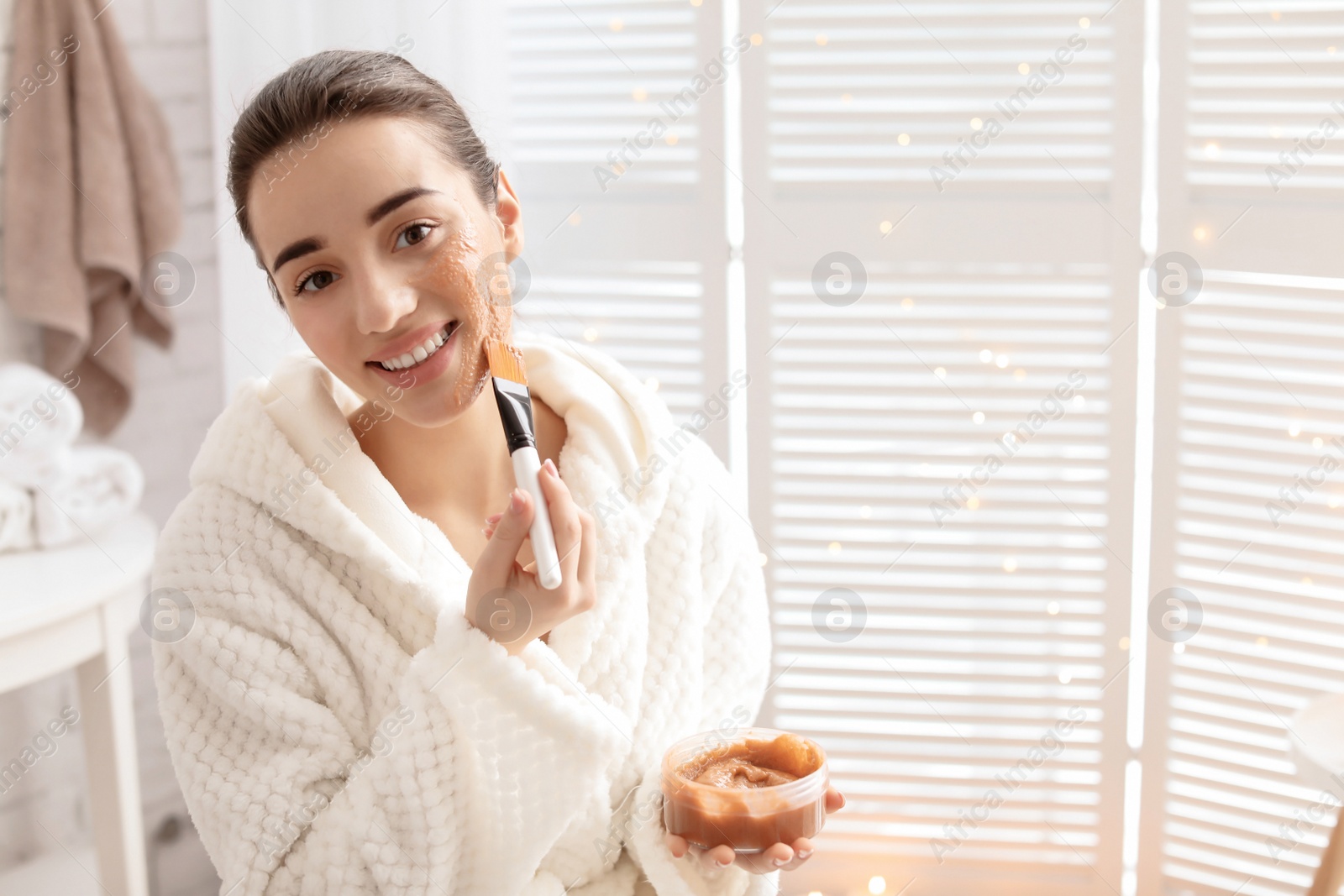 Photo of Young woman applying natural scrub on face in bathroom
