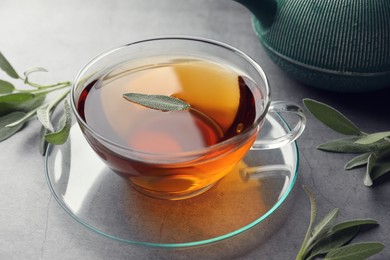 Photo of Cup of aromatic herbal tea with sage on grey table