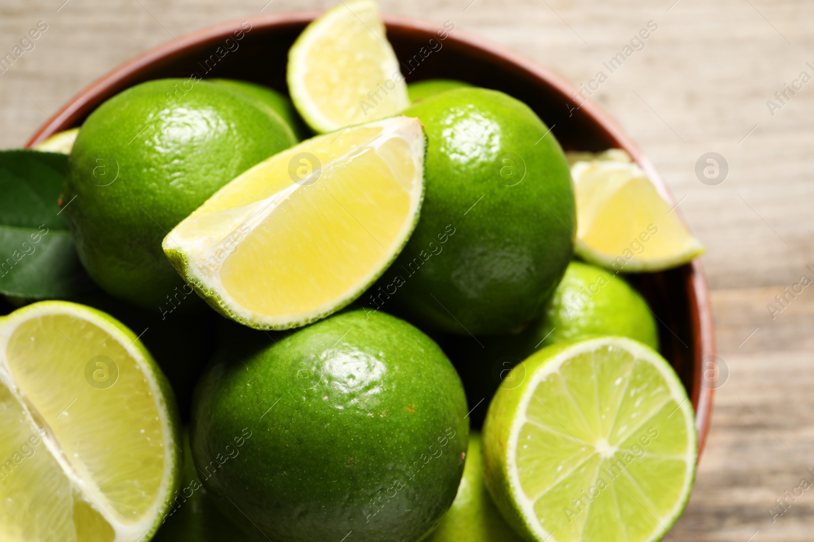Photo of Tasty ripe limes in bowl on wooden table, top view