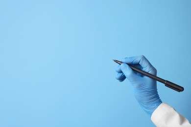 Doctor wearing medical glove writing something on light blue background, closeup. Space for text