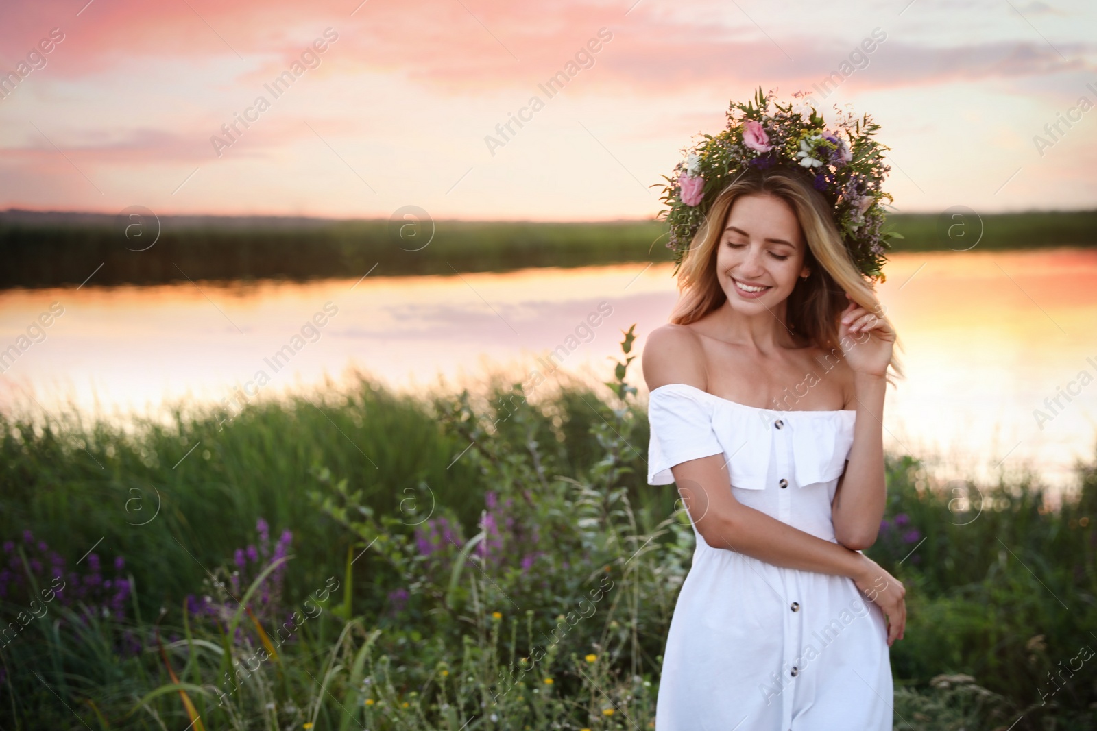 Photo of Young woman wearing wreath made of beautiful flowers outdoors at sunset