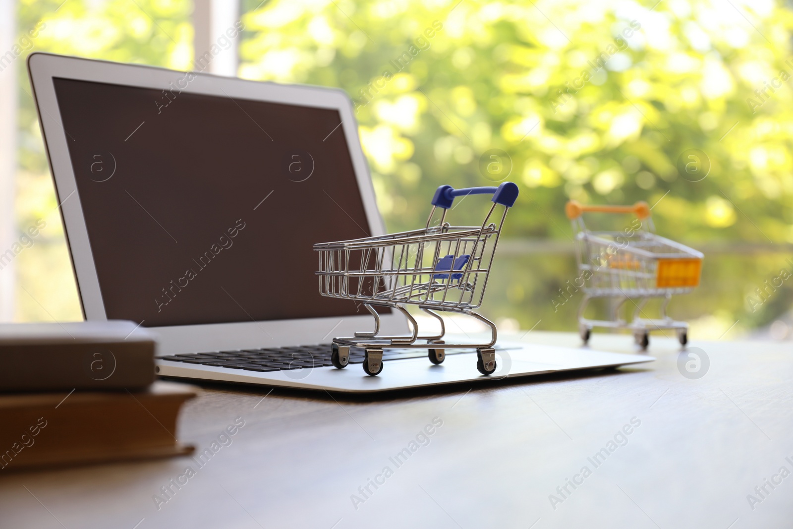 Photo of Internet shopping. Small carts and modern laptop on table indoors