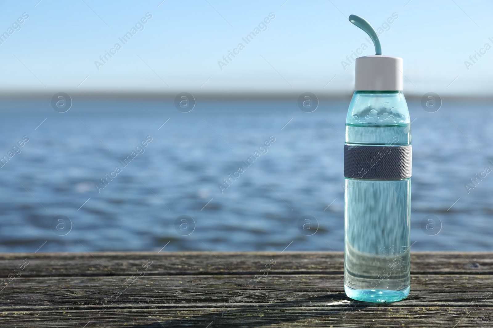 Photo of Glass bottle with water on wooden pier near river outdoors. Space for text