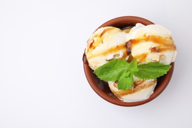 Photo of Tasty ice cream with caramel sauce, mint and nuts in bowl on white background, top view. Space for text