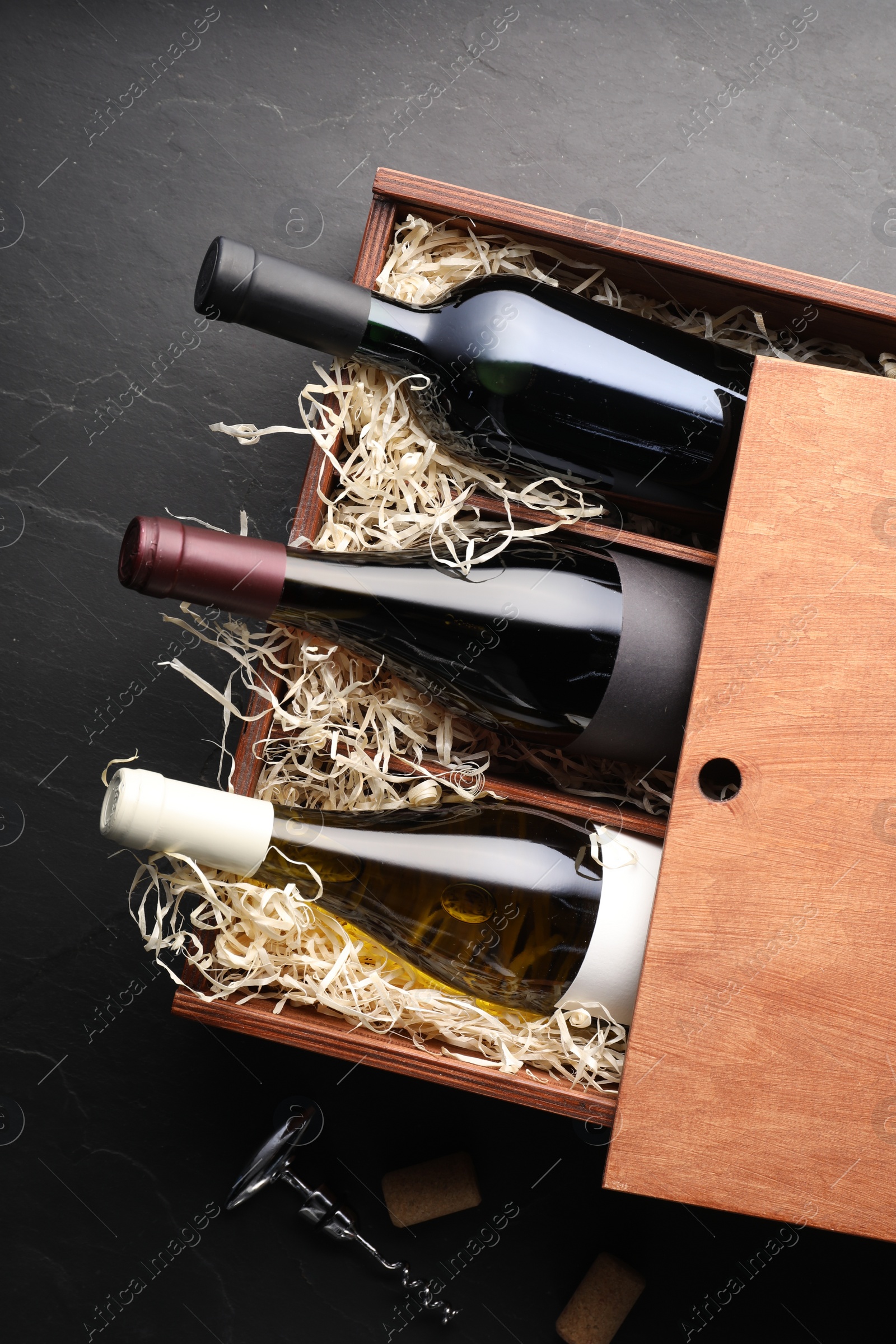 Photo of Box with wine bottles, corkscrew and corks on dark textured table, flat lay