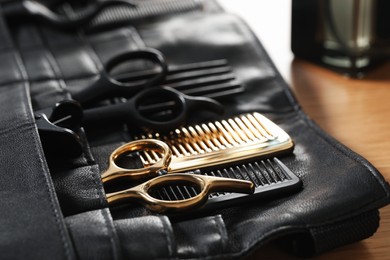 Photo of Hairdresser tools. Professional scissors and combs in leather organizer on wooden table, closeup