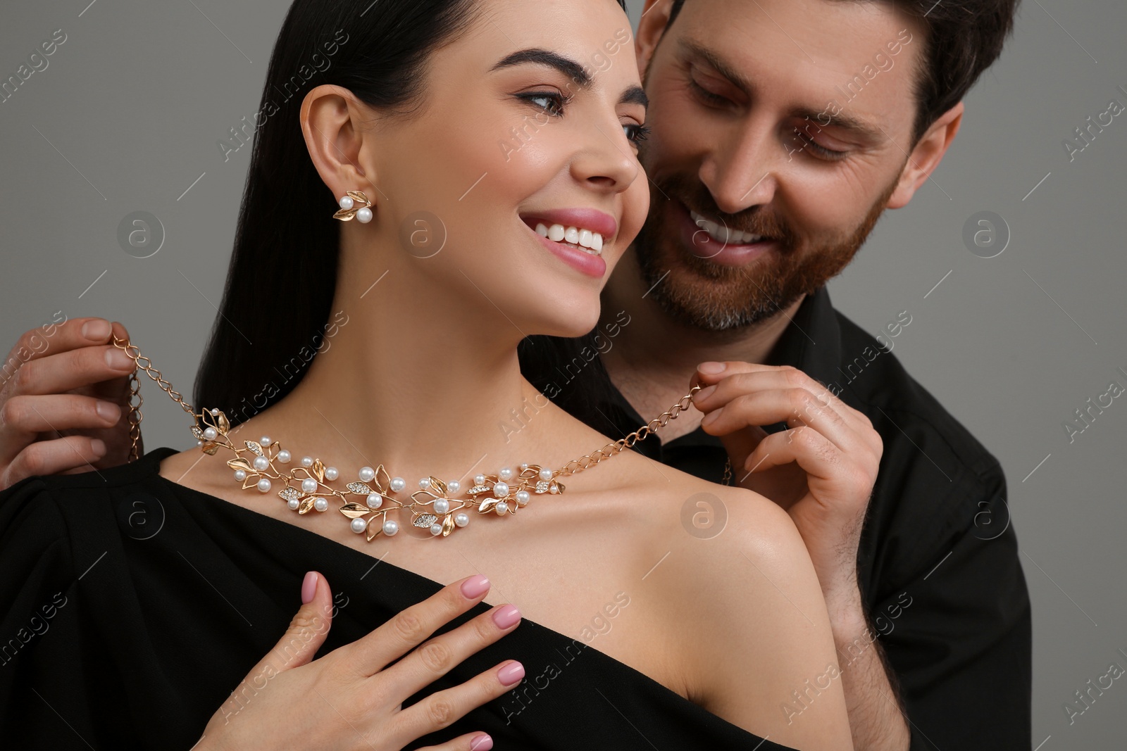 Photo of Man putting elegant necklace on beautiful woman against grey background, closeup