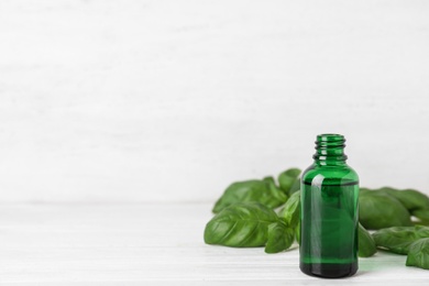 Bottle of basil essential oil on white wooden table against light background. Space for text