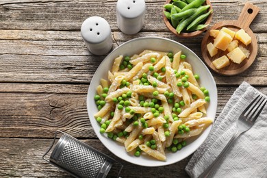 Photo of Delicious pasta with green peas, cheese, grater and fork on wooden table, top view. Space for text