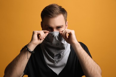 Young man covering his face with bandana on yellow background