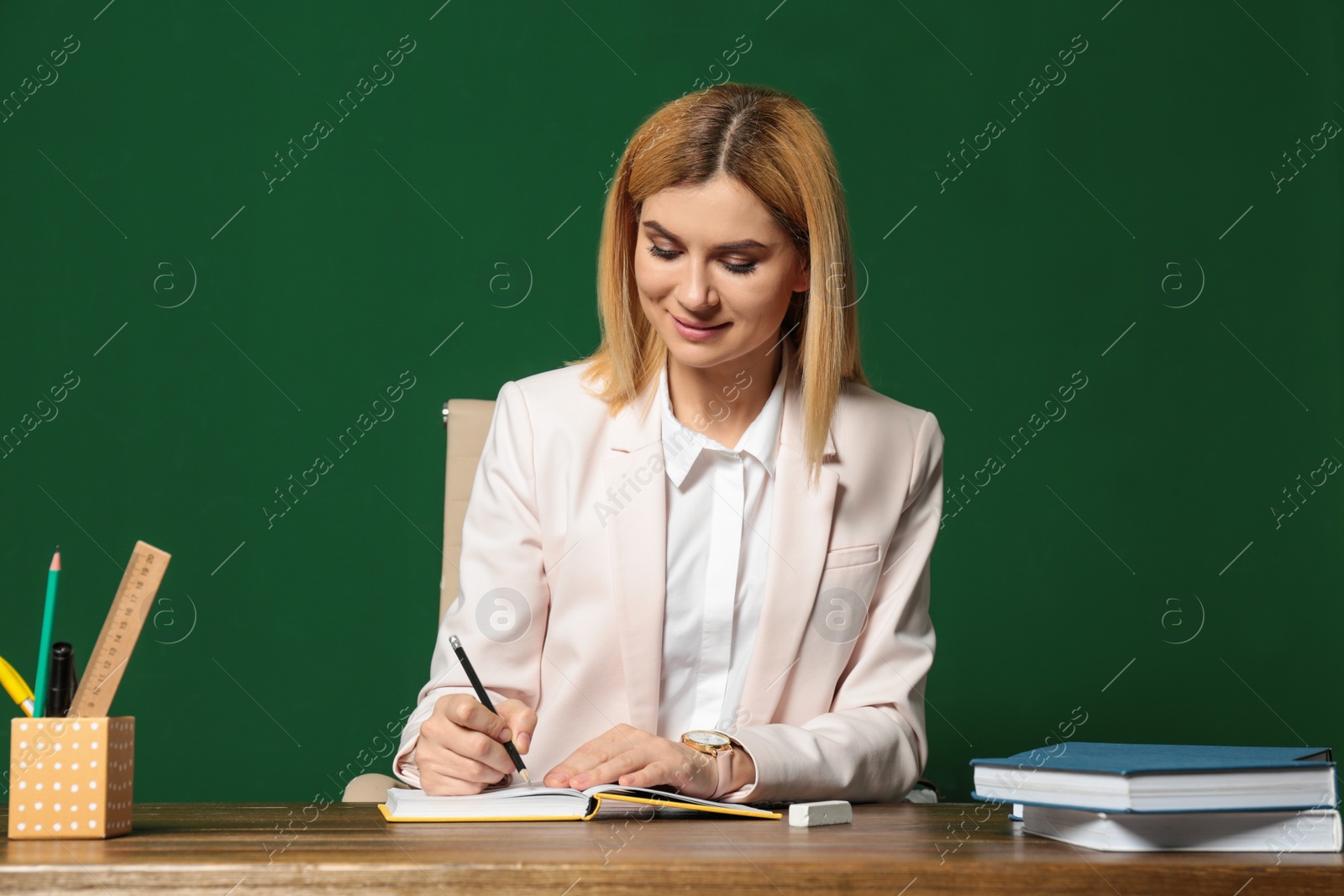 Photo of Portrait of beautiful teacher sitting at table near chalkboard