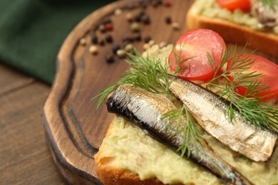 Photo of Delicious sandwich with sprats, tomato, dill and avocado puree on wooden table, closeup. Space for text