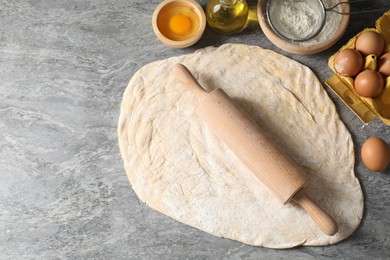 Photo of Raw dough, rolling pin and ingredients on grey table, top view. Space for text