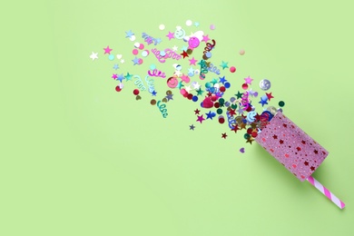 Colorful confetti with party cracker on light green background, top view. Space for text