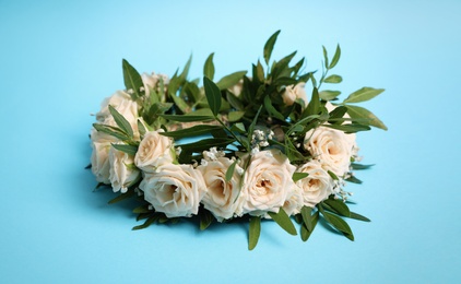 Wreath made of beautiful flowers on light blue background