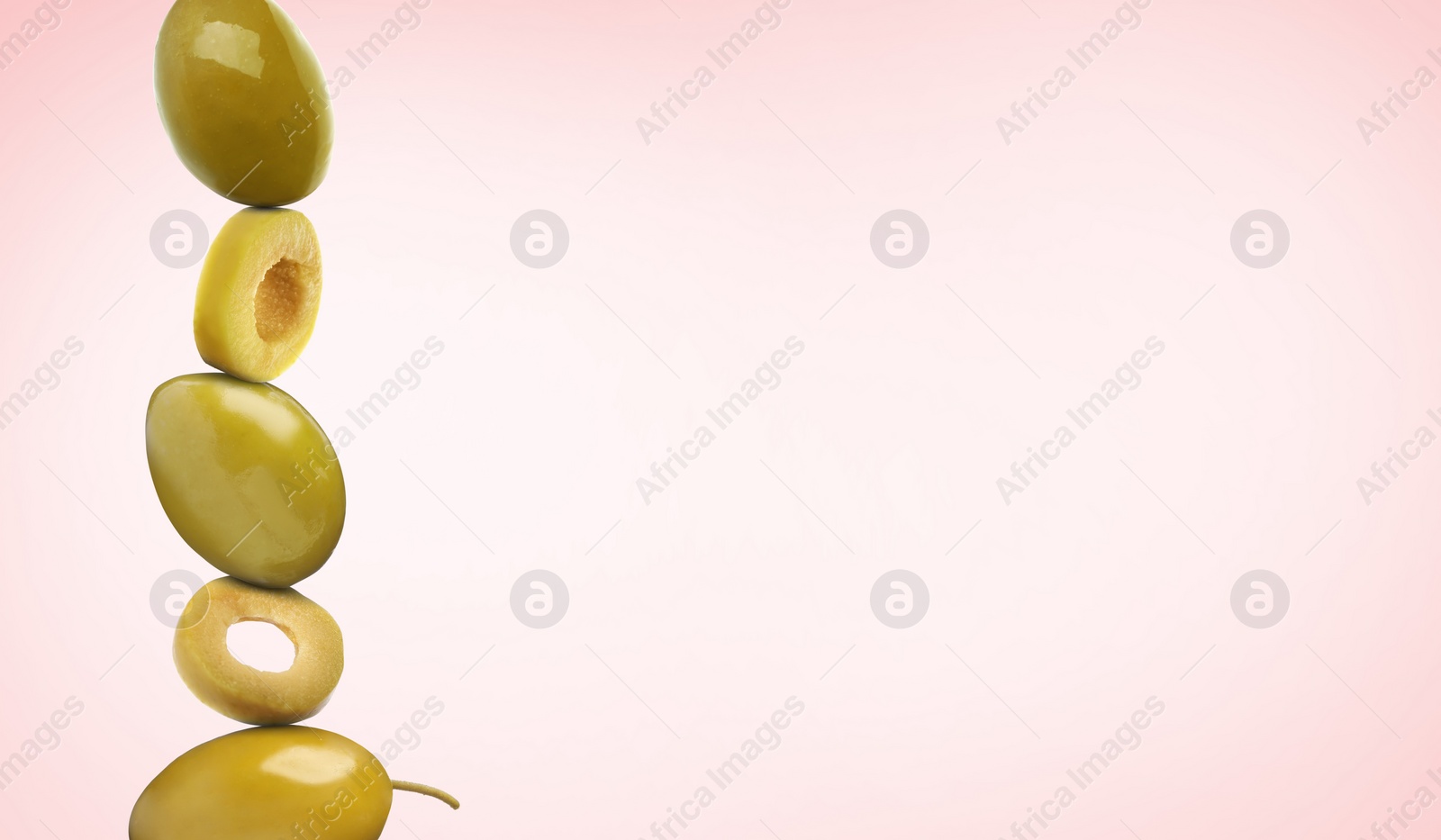 Image of Cut and whole green olives on pink gradient background, space for text