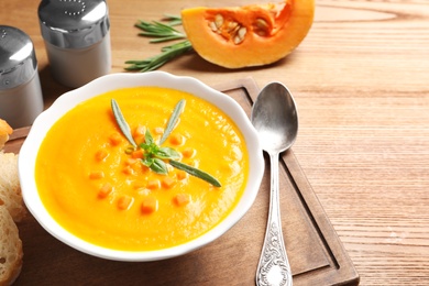 Photo of Bowl with tasty pumpkin soup served on wooden table