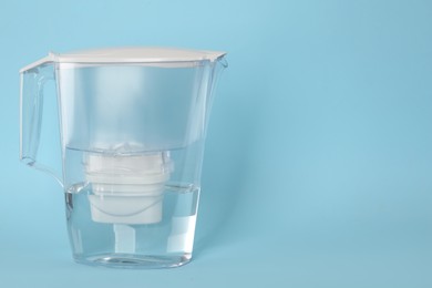 Photo of Filter jug with purified water on light blue background. Space for text