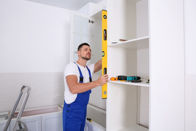 Photo of Worker measuring newly installed kitchen furniture indoors
