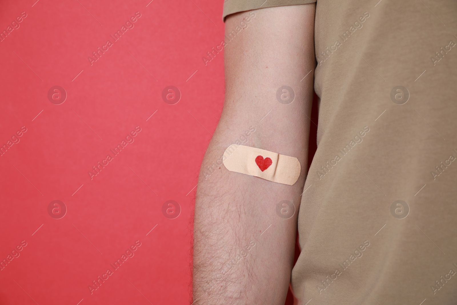 Photo of Blood donation concept. Man with adhesive plaster on arm against red background, closeup. Space for text