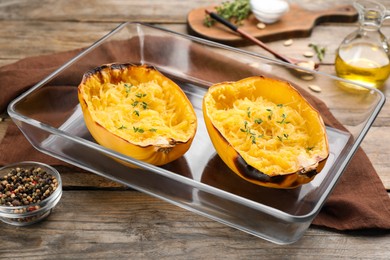 Photo of Halves of cooked spaghetti squash with thyme in baking dish on wooden table