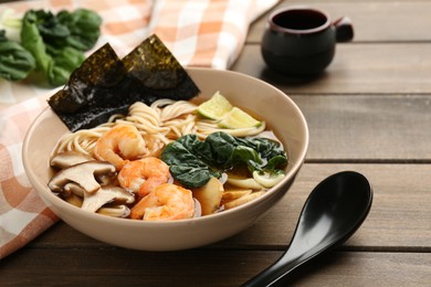 Photo of Delicious ramen with shrimps and mushrooms in bowl served on wooden table, closeup. Noodle soup