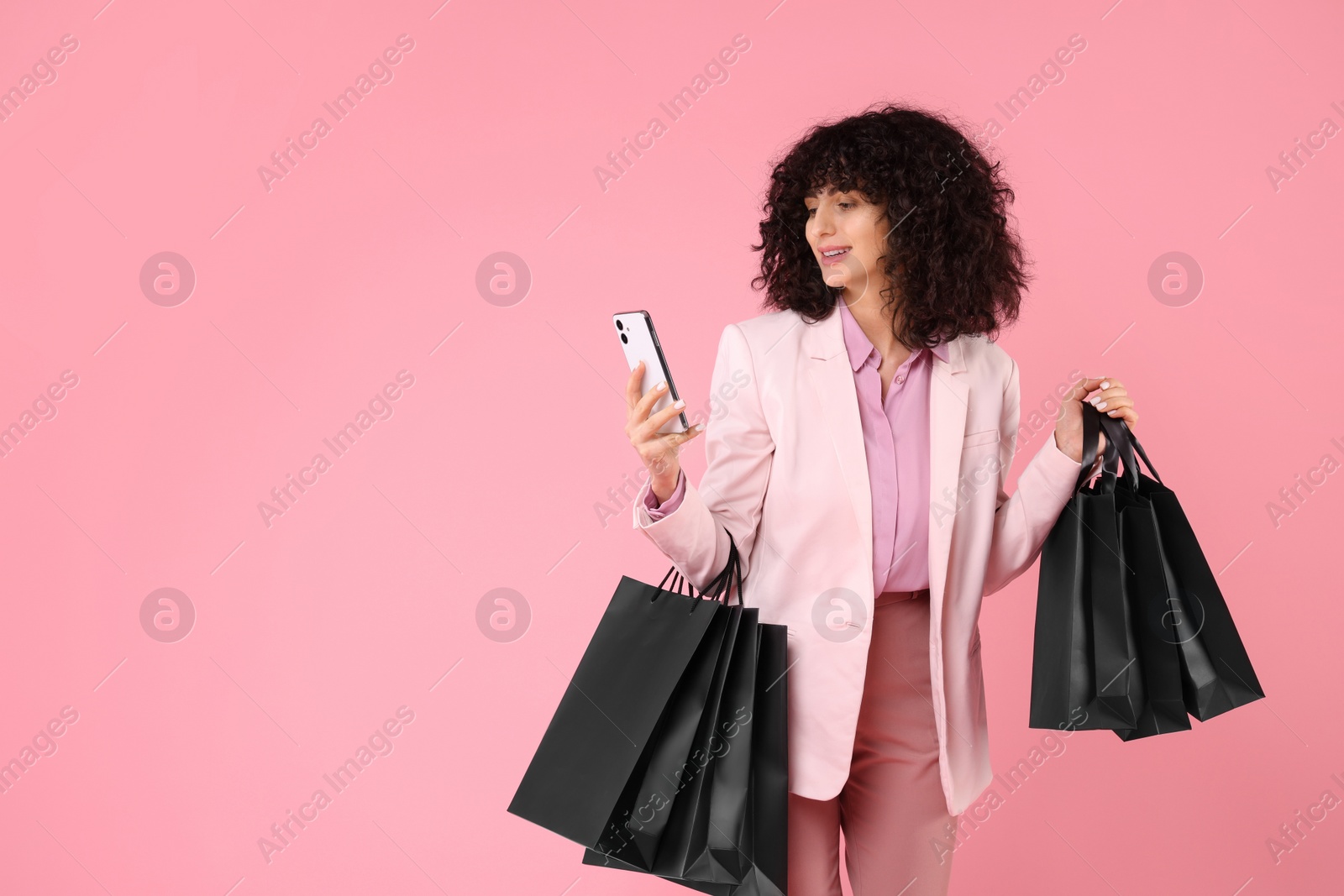 Photo of Happy young woman with shopping bags and modern smartphone on pink background. Space for text