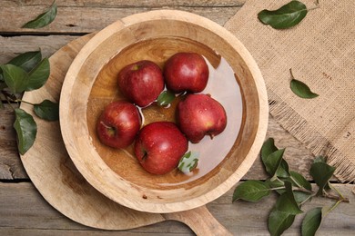 Photo of Fresh red apples in bowl with water and leaves on wooden table, flat lay