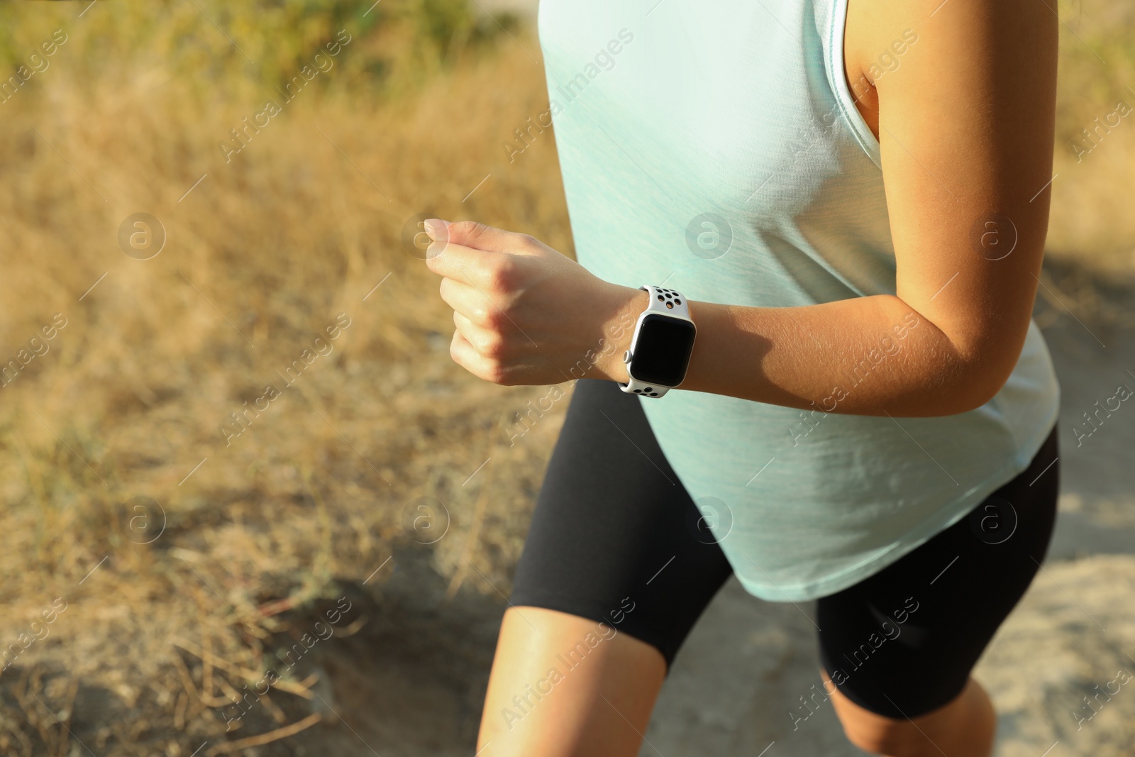 Photo of Woman wearing modern smart watch during training outdoors, closeup