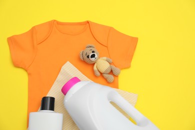 Bottles of laundry detergents, baby clothes and toy bear on yellow background, flat lay. Space for text