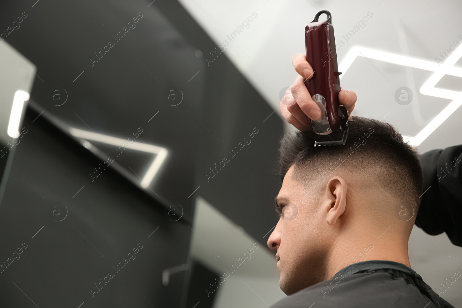 Photo of Professional barber making stylish haircut in salon, closeup