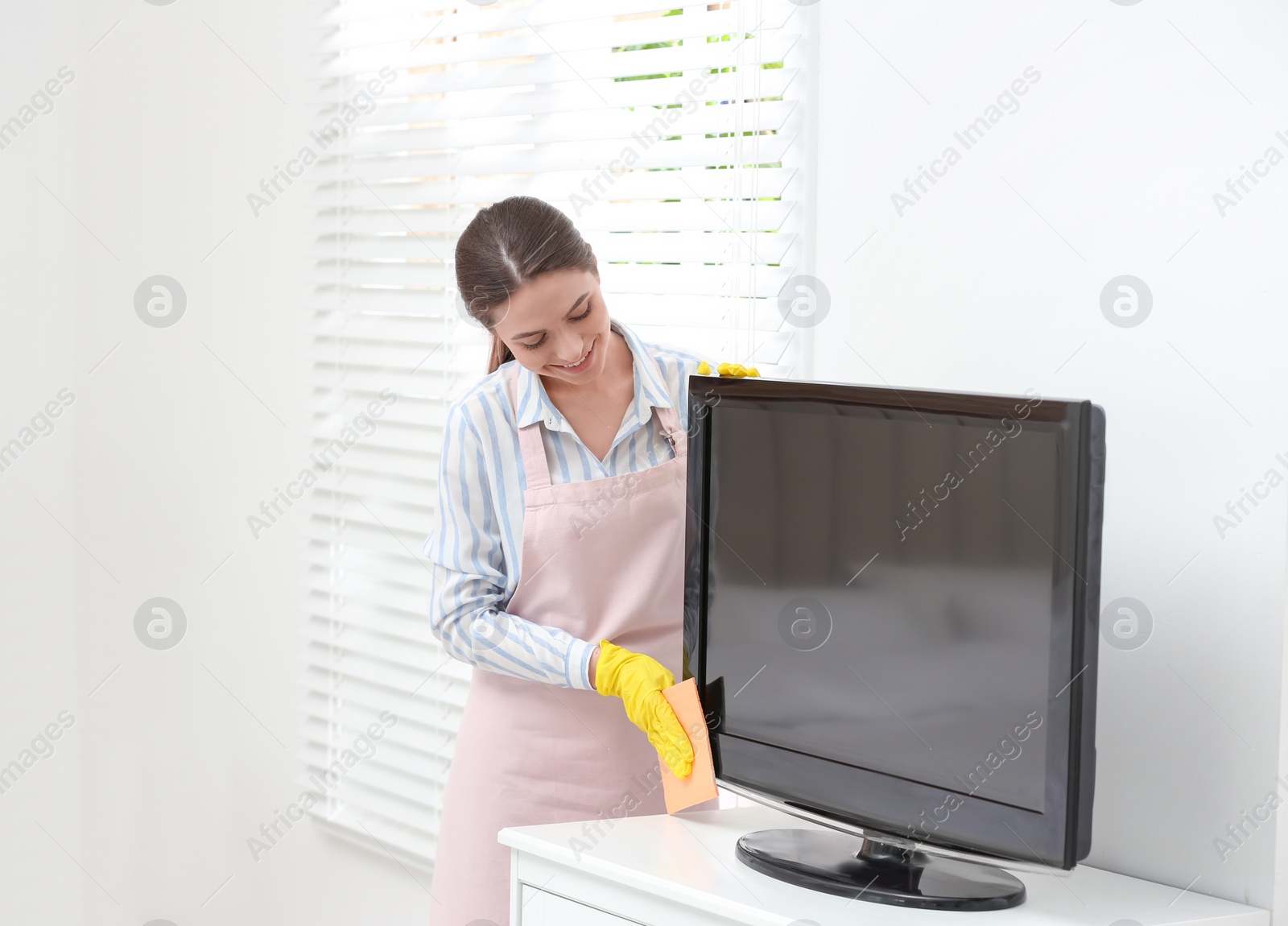 Photo of Young chambermaid wiping dust from TV with rag in hotel room