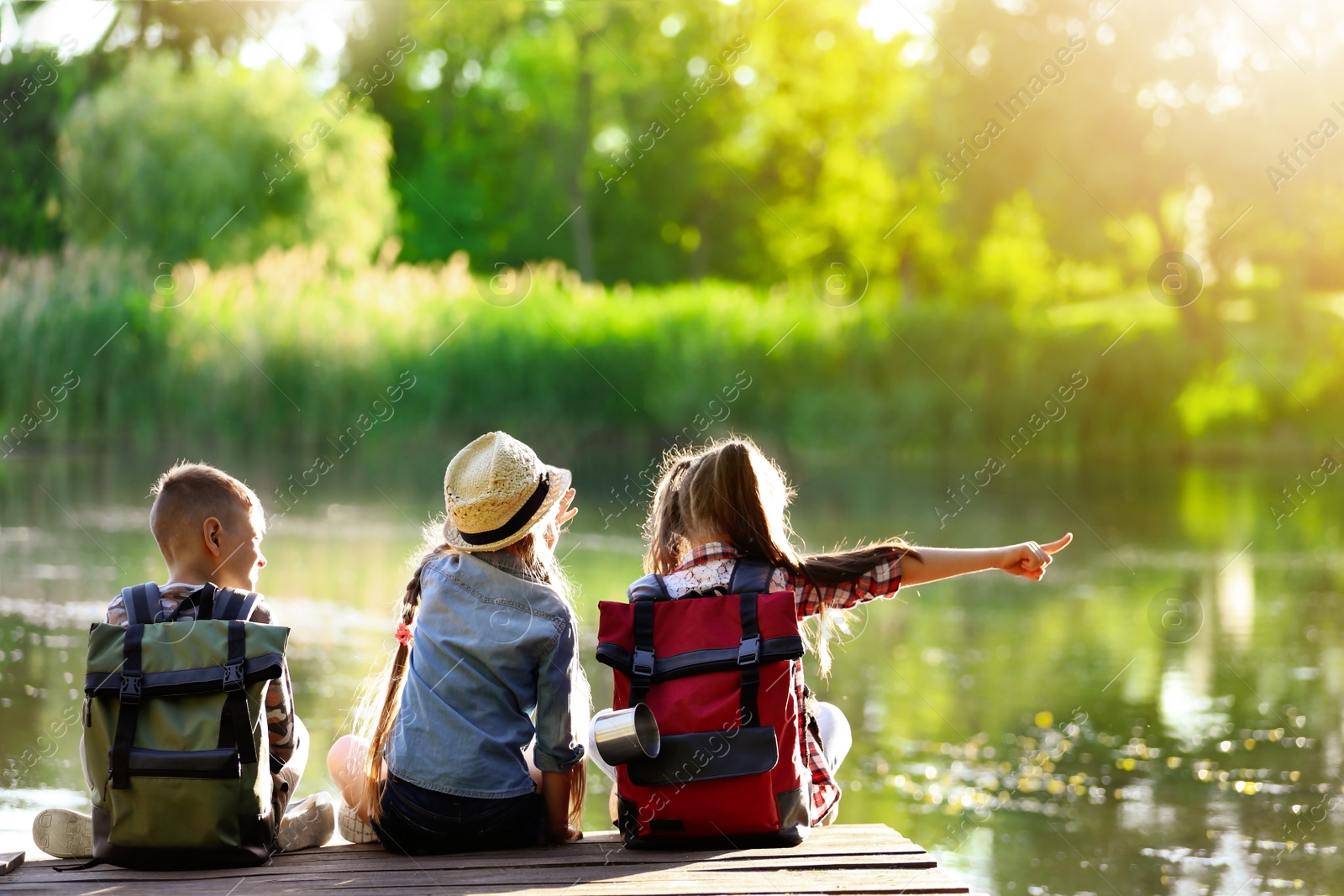 Image of School holidays. Group of children sitting on wooden pier near river 