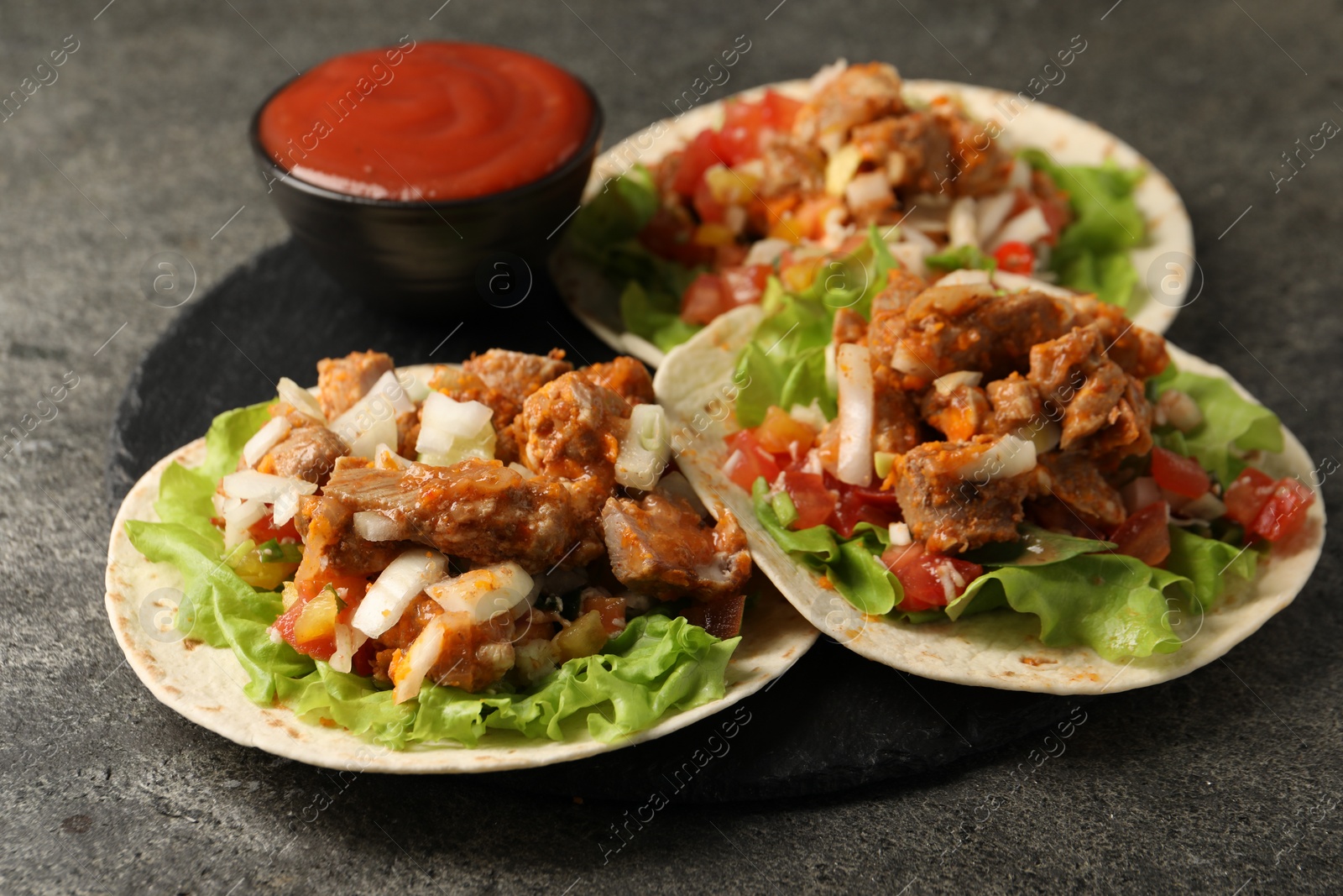 Photo of Delicious tacos with vegetables, meat and ketchup on grey textured table, closeup