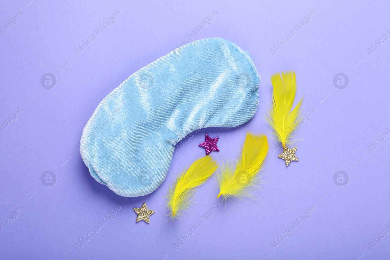 Photo of Soft sleep mask, confetti in shape of stars and feathers on purple background, flat lay