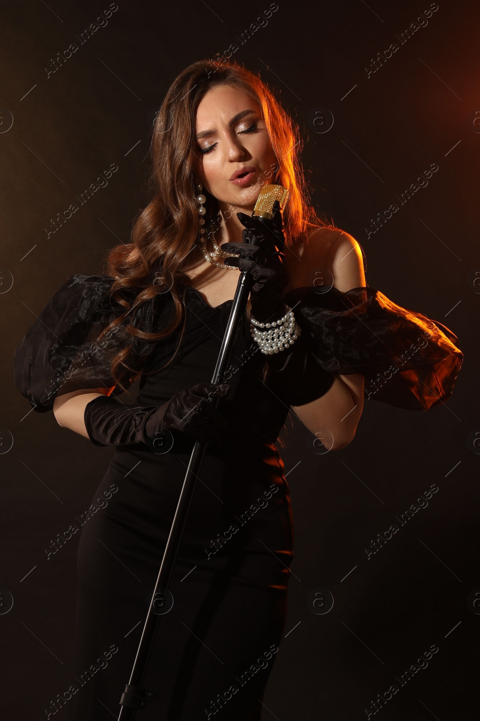 Photo of Beautiful young woman in stylish dress with microphone singing on dark background