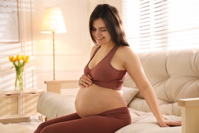 Pregnant young woman touching belly at home