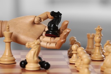 Photo of Robot with knight over chessboard against light background, closeup. Wooden hand representing artificial intelligence