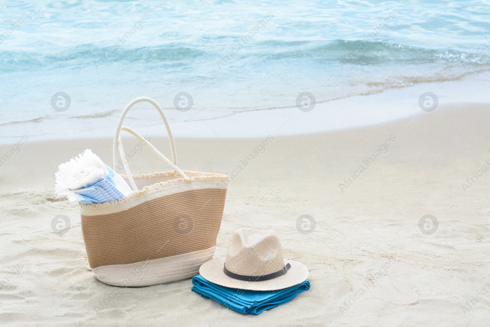 Photo of Bag with blanket, beach towel and straw hat on sandy seashore, space for text