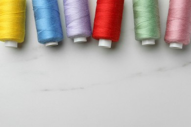 Colorful sewing threads on white marble table, flat lay. Space for text
