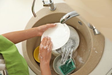 Photo of Woman washing dirty dishes in kitchen sink. Cleaning chores