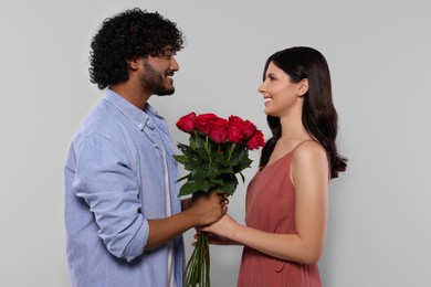 International dating. Happy couple with bouquet of roses on light grey background