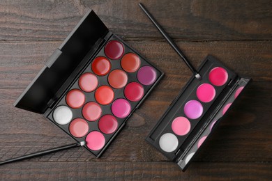 Photo of Colorful lipstick palettes with brushes on wooden table, flat lay. Professional cosmetics