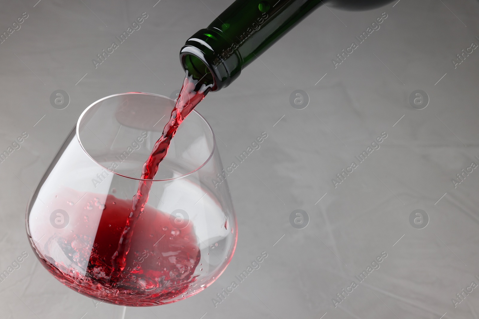 Photo of Pouring tasty red wine in glass at gray table, closeup. Space for text