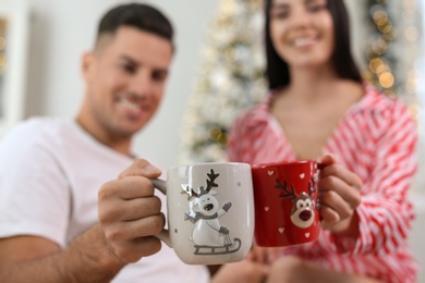 Photo of Couple toasting with cups at home, focus on hands. Christmas celebration