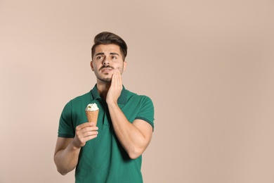 Emotional young man with sensitive teeth and ice cream on color background. Space for text