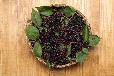 Photo of Elderberries (Sambucus) with leaves in bowl on wooden table, top view