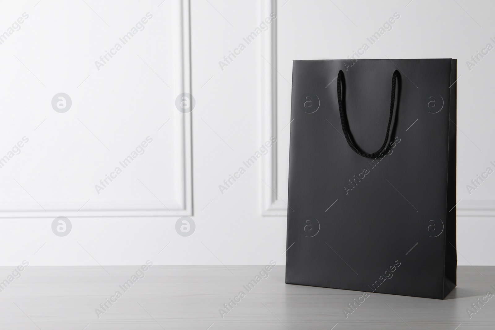 Photo of Black paper bag on white wooden table, space for text