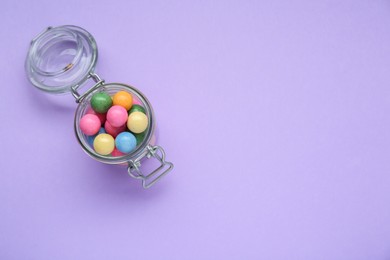 Jar with many bright gumballs on lilac background, top view. Space for text