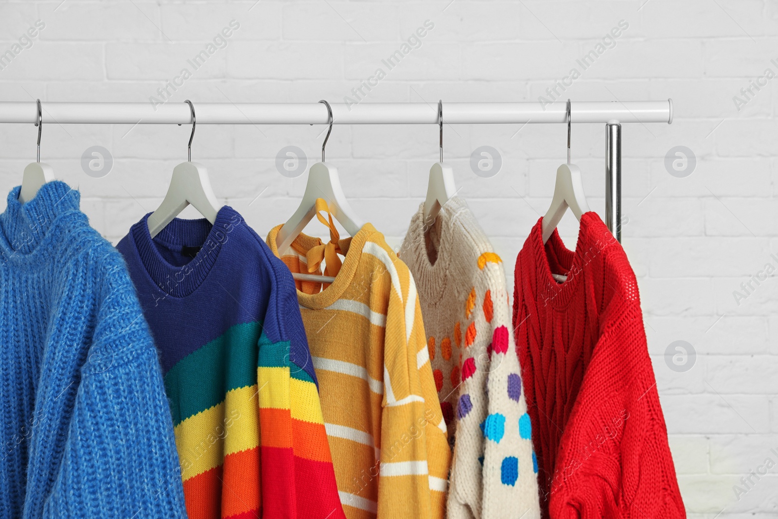 Photo of Collection of warm sweaters hanging on rack against white brick wall